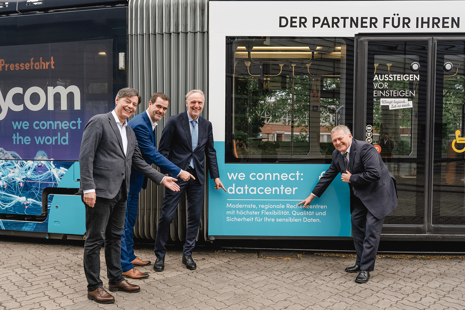 Gruppenfoto vor der Citycom Straßenbahn mit Hainzl, Stockinger, Riegler und Malik, die auf das Branding zeigen.